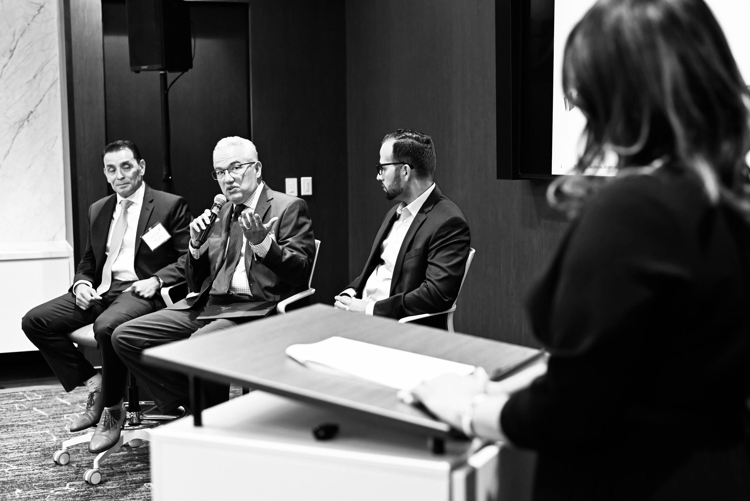 Three men and a woman sitting at a panel discussion. The man in the center is speaking into a microphone